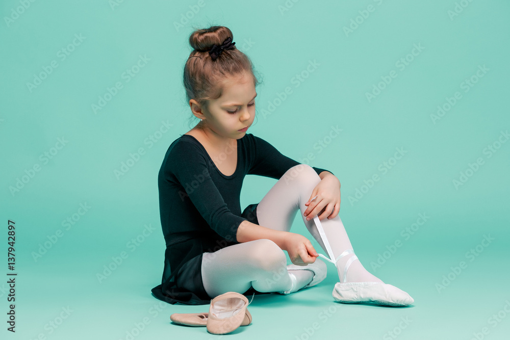 Fototapeta premium Beautiful little ballerina in black dress for dancing puting on foot pointe shoes