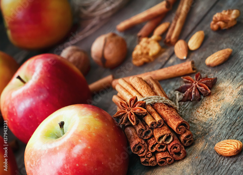 Fresh red and green apples, cinnamon sticks, ground cinnamon, anise stars, walnuts and hazelnuts on an old wooden background