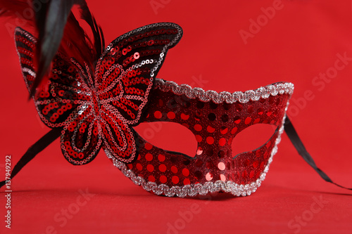 Carnival mask with butterfly and feathers. Red glossy mask on red background.
