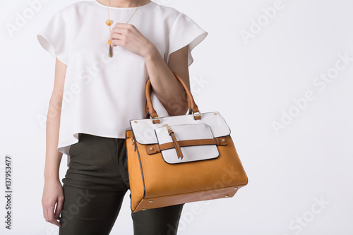 Stylish woman in modern clothes with bright orange white handbag in hands posing at studio isolated on white background
