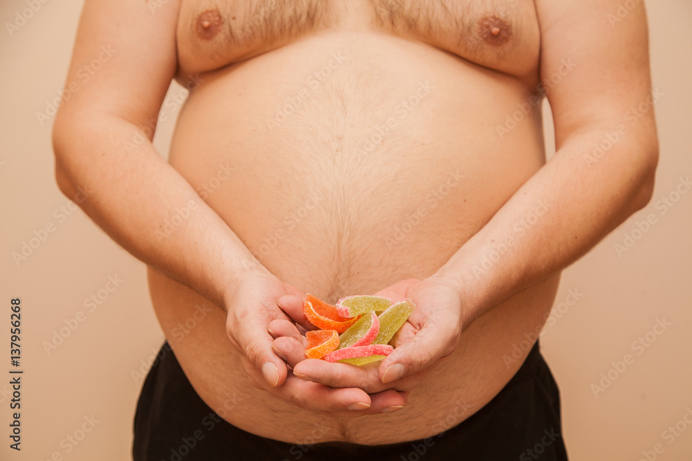 a fat man with overweight holding a handful of sweets a fat man with overweight holding a handful of sweets