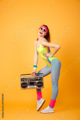 Attractive young sportswoman standing and posing with retro boombox