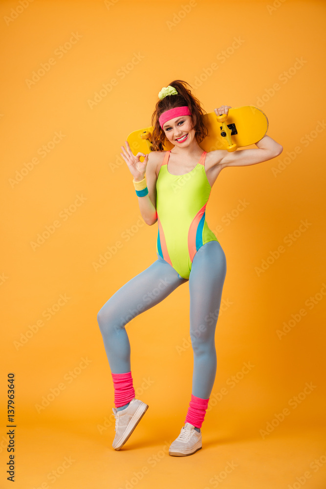 Smiling young woman athlete holding skateboard and showing ok sign Smiling young woman athlete holding skateboard and showing ok sign