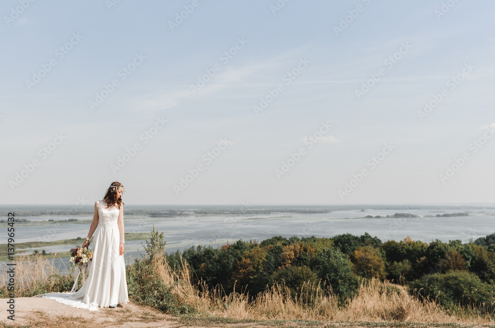 Невеста в свадебном платье на горе с видом на просторный разлив реки