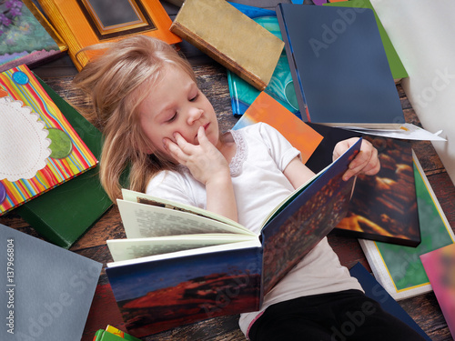 child and a lot of books around. Little girl reading a book lying on the floor