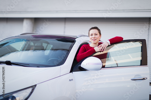 A young woman in red jumper with her white car.