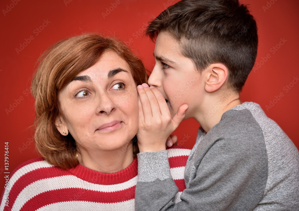 Young boy whispering secret into ears of smiling mother Young boy whispering secret into ears of smiling mother