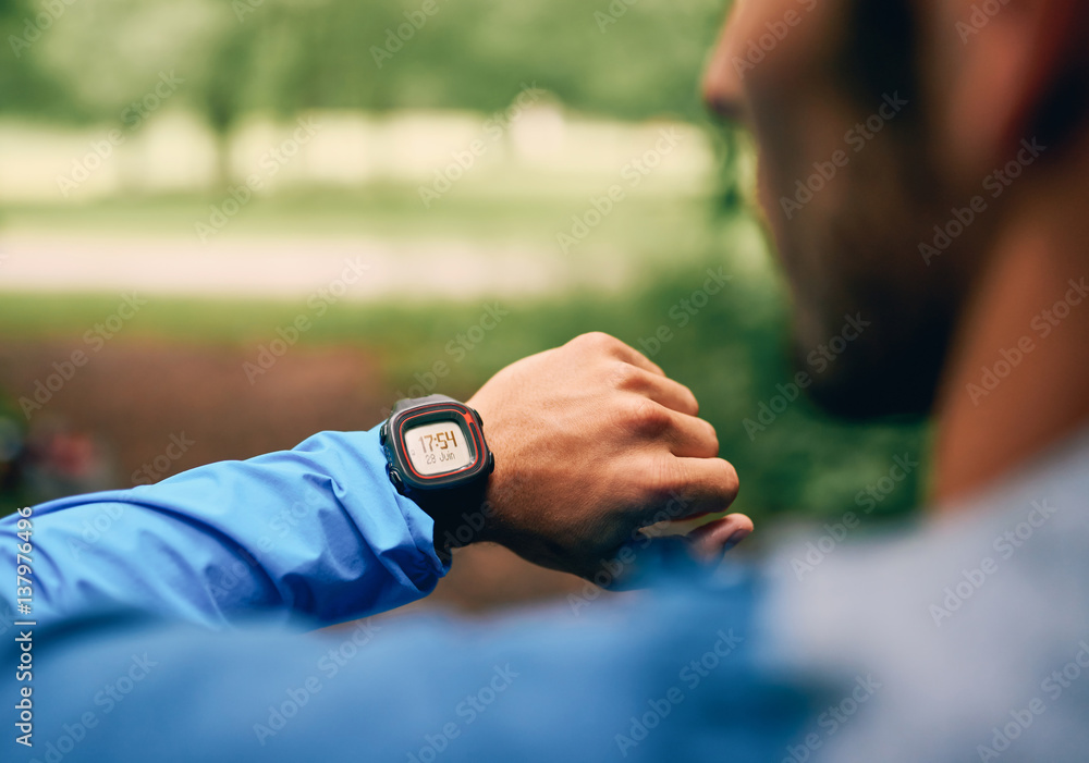 Fit male jogger day using a smartwatch during cross country forest trail race in a nature park.