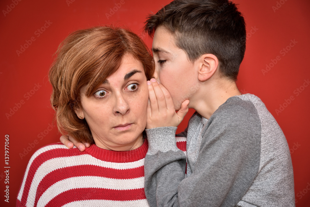 Young boy whispering secret into ears of surprised mother Young boy whispering secret into ears of surprised mother