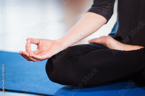 Yoga girl meditating indoor and making a zen symbol with her hand. Closeup of woman body in yoga pose on a green mat