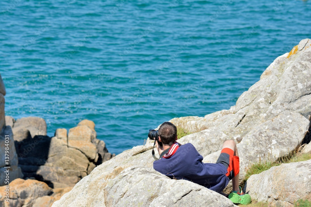 Un homme est allongé sur un rocher pour prendre une photo