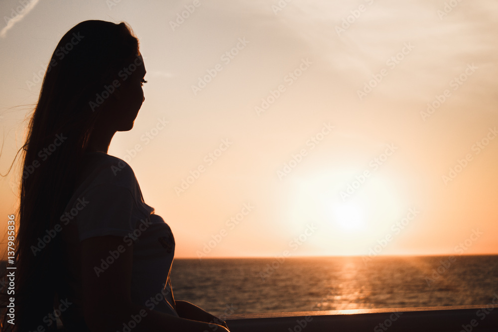 Beautiful girl looks at the sea a fiery sunset. Silhouette of a girl
