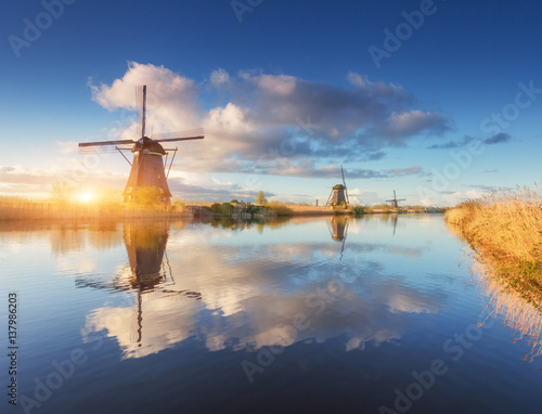 Windmills at sunrise. Rustic landscape with amazing dutch windmills near the water canals with blue sky and clouds reflected in water. Beautiful morning in Kinderdijk, Netherlands in spring. Travel