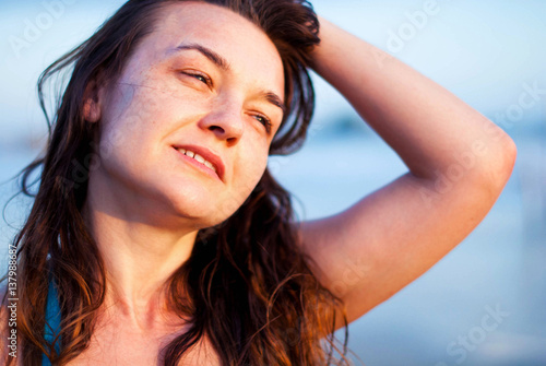 Young happy girl with freckles and long hair smiling at the beach during sunset.