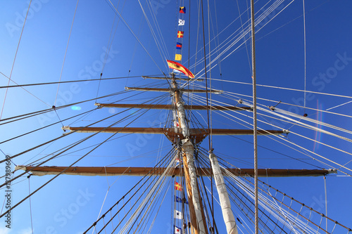 A sailing ship mast with ropes against blue sky and patch of reflected light from sun