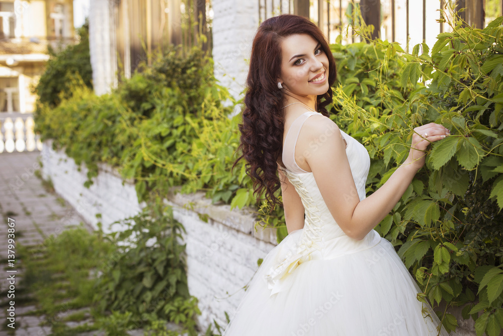 Beautiful brunette woman bride in a garden park in white wedding dress, curly hairstyle and a smile. warm weather, outdoors. copy space Beautiful brunette woman bride in a garden park in white wedding dress, curly hairstyle and a smile. warm weather, outdoors. copy space