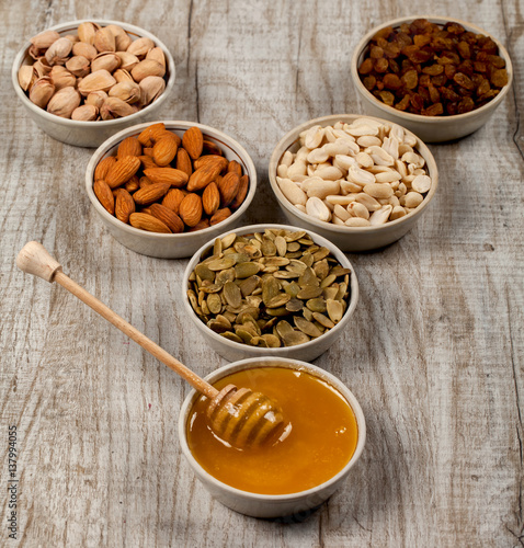 Pistachios, almonds, peanuts, pumpkin seeds, raisins and honey in ceramic plates.