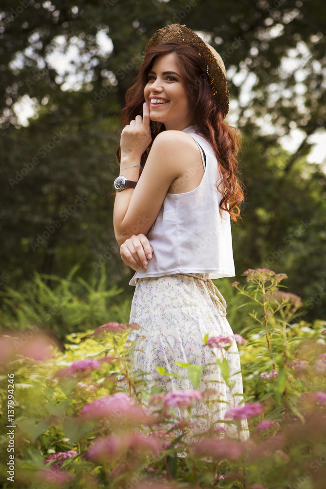 Young beautiful caucasian white brunette woman with curly hairstyle and make up, in a summer outfit: dress and a hat in park. outdoors Young beautiful caucasian white brunette woman with curly hairstyle and make up, in a summer outfit: dress and a hat in park. outdoors