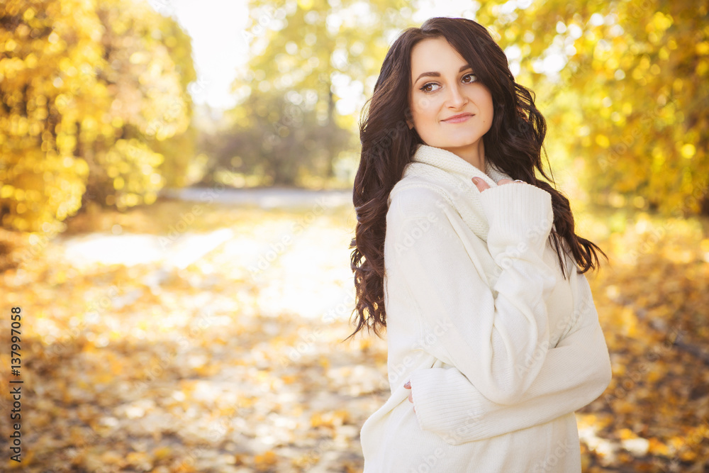 Beautiful caucasian brunette young woman in warm autumn day at park. Yellow leaves and sunshine. Fall season. Woman in white sweater, smiling. Copy space Beautiful caucasian brunette young woman in warm autumn day at park. Yellow leaves and sunshine. Fall season. Woman in white sweater, smiling. Copy space