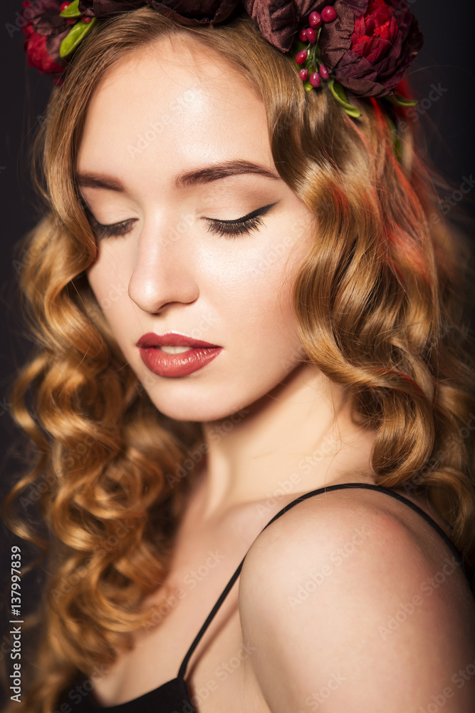 Beautiful blonde model woman with curly hairstyle and black cat eyes, in black dress with circlet (wreath) of flowers (roses) on her head. her eyes closed, showing make up. black background. close-up Beautiful blonde model woman with curly hairstyle and black cat eyes, in black dress with circlet (wreath) of flowers (roses) on her head. her eyes closed, showing make up. black background. close-up