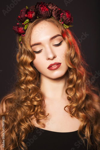 Beautiful blonde model woman with curly hairstyle and black cat eyes, in black dress with circlet (wreath) of flowers (roses) on her head. her eyes closed, showing make up. black background. close-up