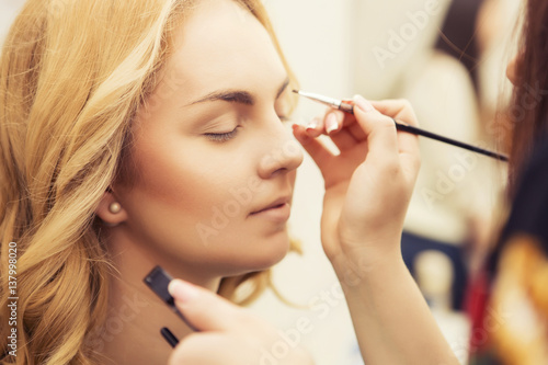 Brunette make up artist woman applying make up for a blonde bride in her wedding day, for a date
