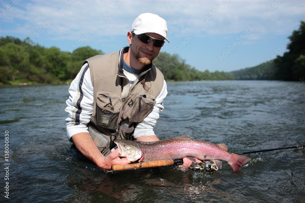 Huchen / Fisherman standing in deep water presenting caught Danube salmon. Spin fishing in San River, Sub-Carpathian region. The huchen occurs also in Danajec River. Huchen / Fisherman standing in deep water presenting caught Danube salmon. Spin fishing in San River, Sub-Carpathian region. The huchen occurs also in Danajec River.