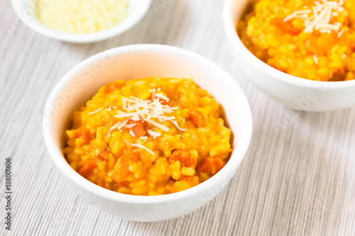 Fresh homemade carrot risotto made with pureed carrot and roasted carrot pieces, garnished with grated cheese, photographed with natural light (Selective Focus, Focus in the middle of the risotto)