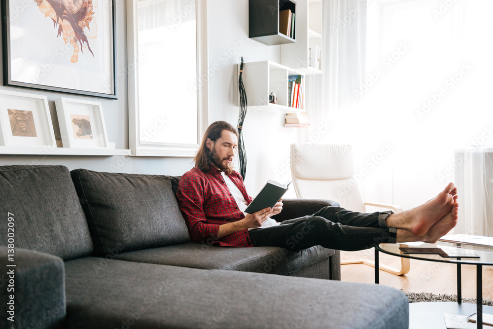 Handsome man sitting and reading book on sofa at home Handsome man sitting and reading book on sofa at home