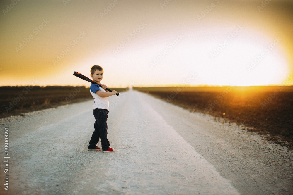 Portrait of boy holding baseball bat while standing on road amidst field against sky during sunset Portrait of boy holding baseball bat while standing on road amidst field against sky during sunset