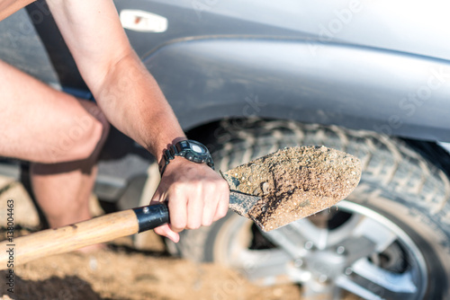 a man digs a car stuck in the sand, throwing sand shovel out from under the car