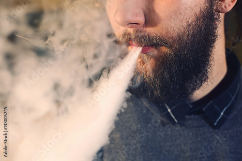 Men with beard vaping and releases a cloud of vapor. close-up.