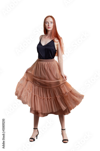Beautiful young long skinny model with red hair wearing bronze color transparent pleated skirt and black silk top