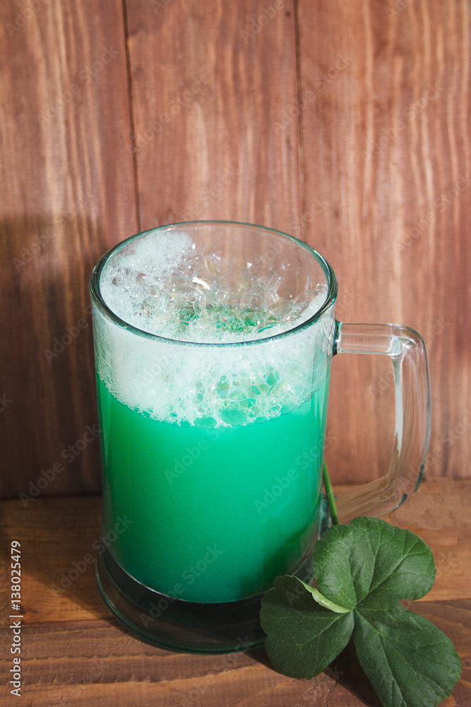 St Patrick's Day concept. Mug of green beer and a three-leaf clover against a wooden background St Patrick's Day concept. Mug of green beer and a three-leaf clover against a wooden background