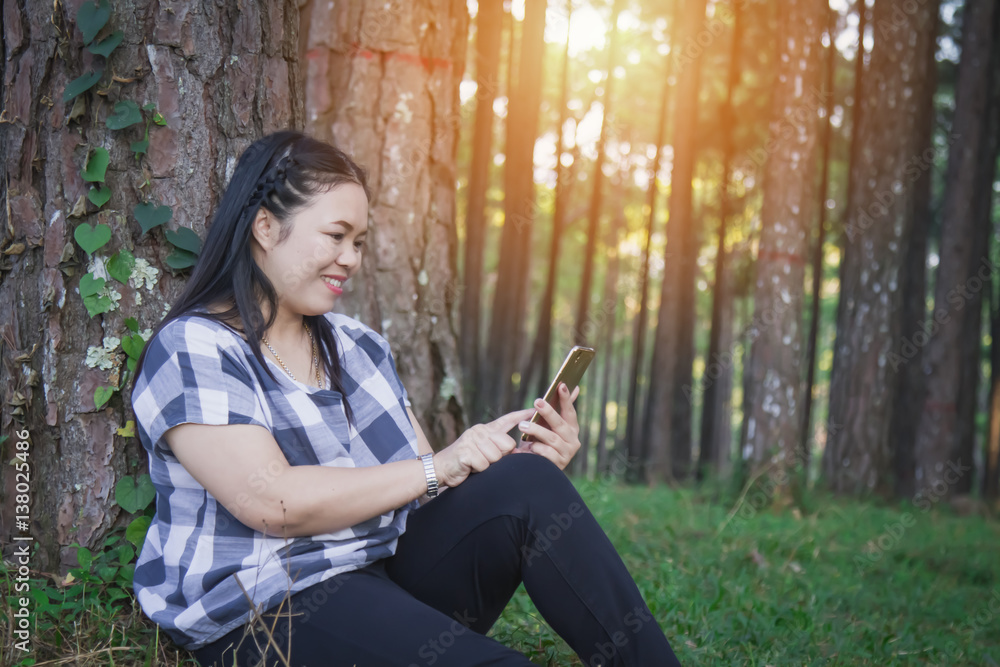 Asia woman relax sit on grass use smart phone in wood forest with copy space. Soft flare sunlight. Asia woman relax sit on grass use smart phone in wood forest with copy space. Soft flare sunlight.