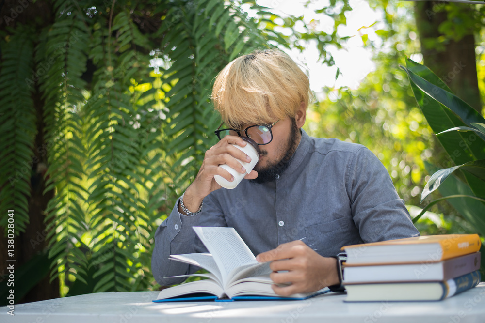 Young hipster beard man drinking coffee while reading books in home garden with nature. Education concept. Young hipster beard man drinking coffee while reading books in home garden with nature. Education concept.