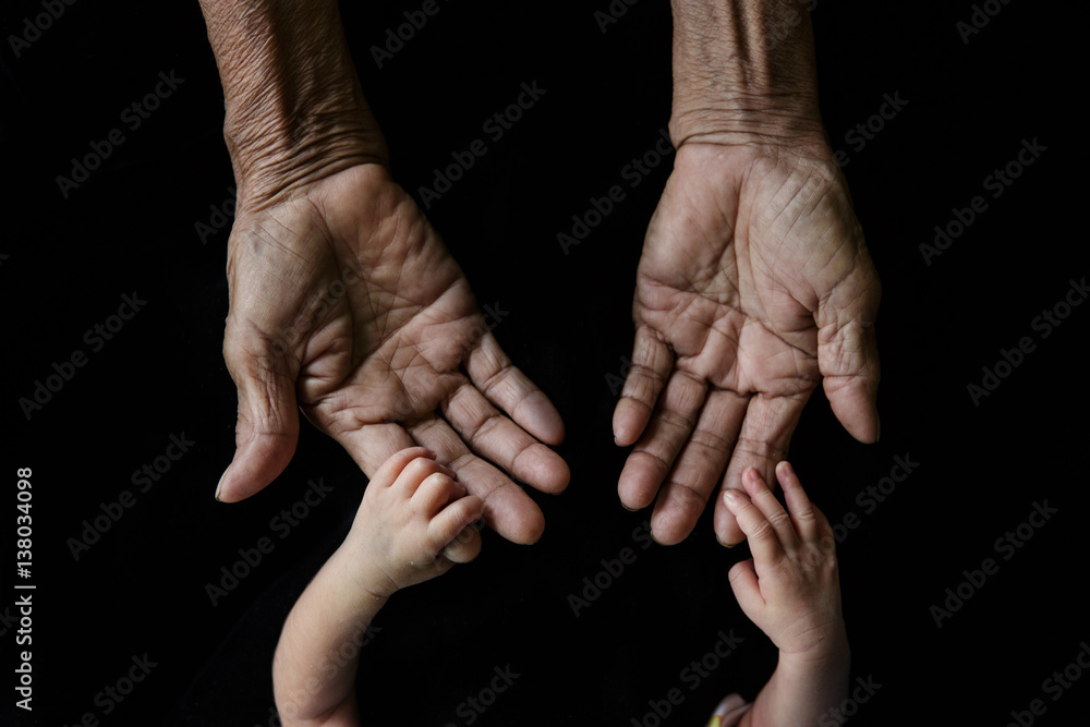 Fototapeta premium Hand of a young baby touching old hand of the elderly (Soft focus and blurry)