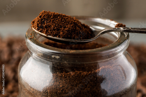 Ground coffee in metal spoon on a glass jar