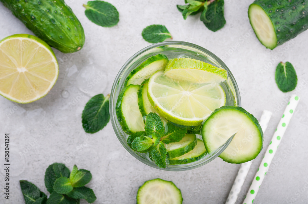 Refreshing water with cucumber, mint and lime on grey background top view. Summer cocktail cucumber lemonade. Healthy drink and detox concept Refreshing water with cucumber, mint and lime on grey background top view. Summer cocktail cucumber lemonade. Healthy drink and detox concept