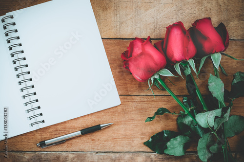 Red roses, leather notebook, pen and cup of coffee on wooden background with copy space.Valentines Day background concept, Wedding day.Top view vintage tone photo