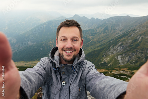 Smiling hiker taking a selfie in front of mountain landscape photo
