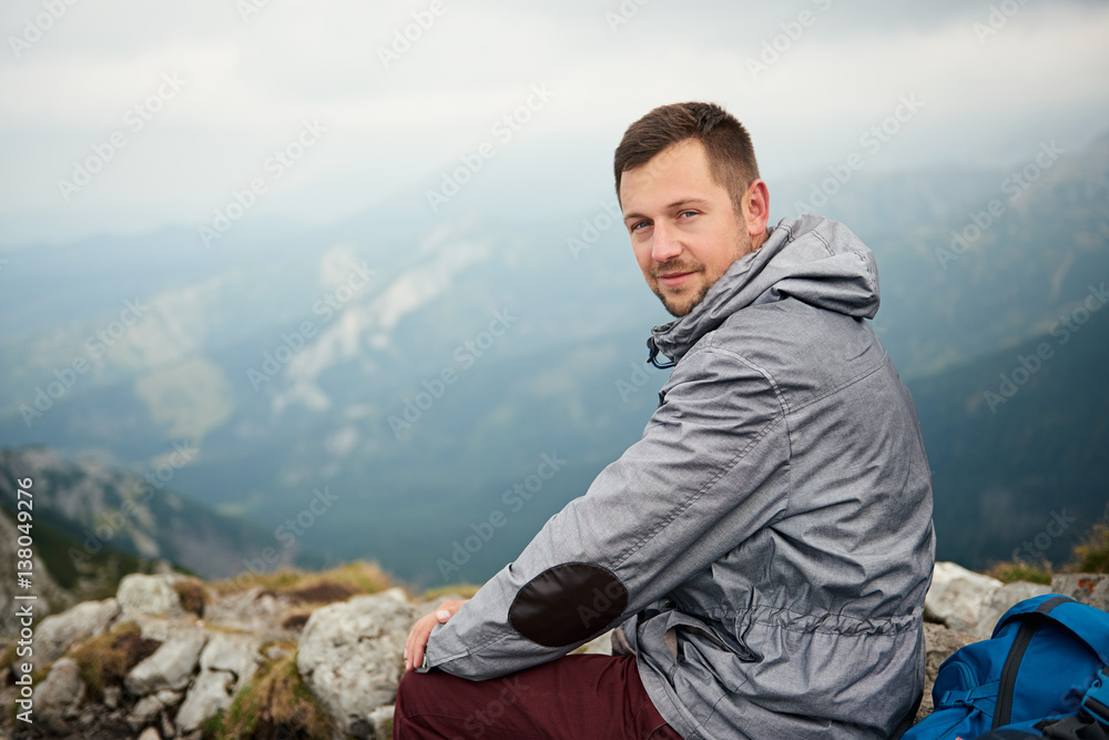 Man sitting on atop a mountain with landscape behind him