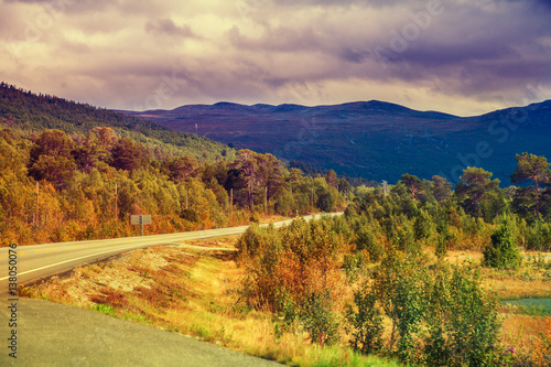 Mountain road at sunset with dramatic cloudy sky. Beautiful nature Norway. Colorful autumn. Mountain landscape.