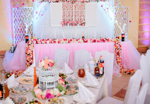 Long dinner table decorated with pink clothes and flowers waits for newlyweds in restaurant