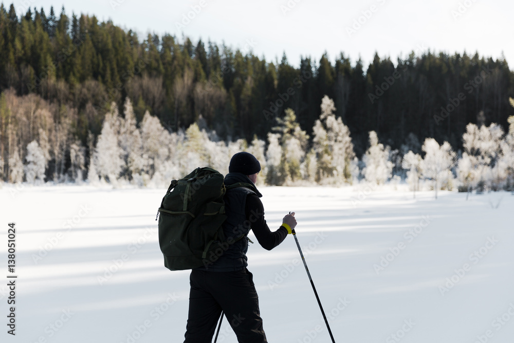 Skier tourist with a backpack on a frozen lake in the woods around the sun