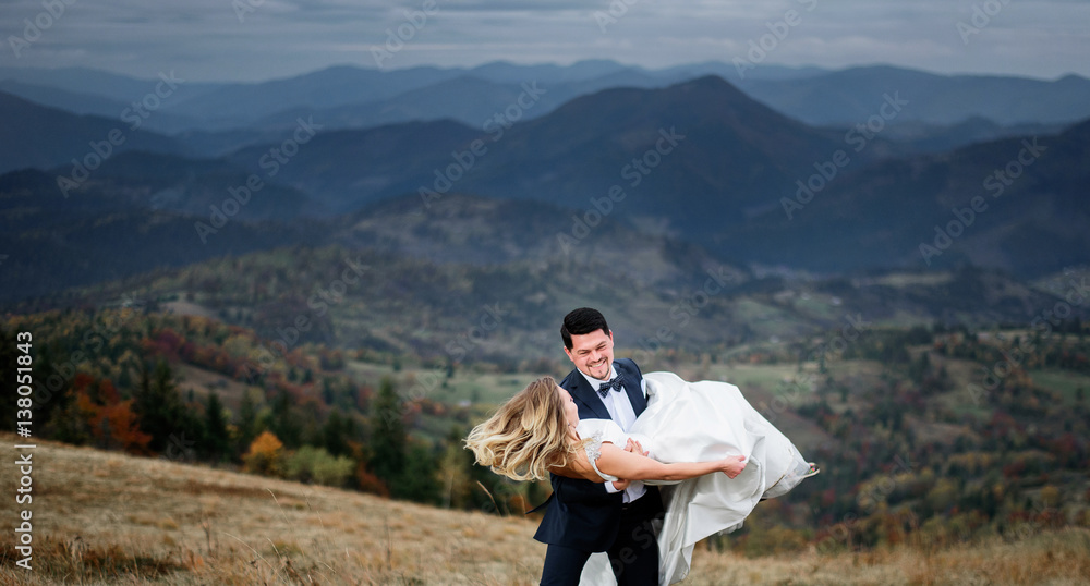 Groom whirls bride on mountain hill holding her tender in his arms