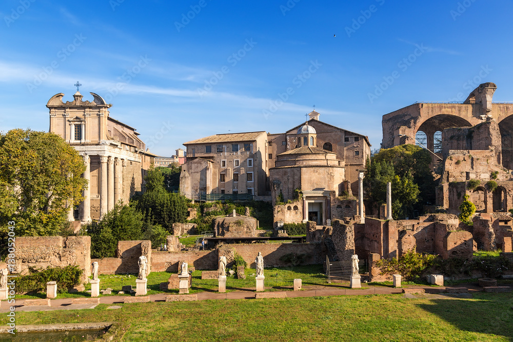 Rome, Italy. In foreground - ruins of portico with statues of  House of Vestals. In background: Temple of Antoninus and Faustina (141 AD), Temple of Romulus (307 AD),  Basilica of Maxentius, 308 AD