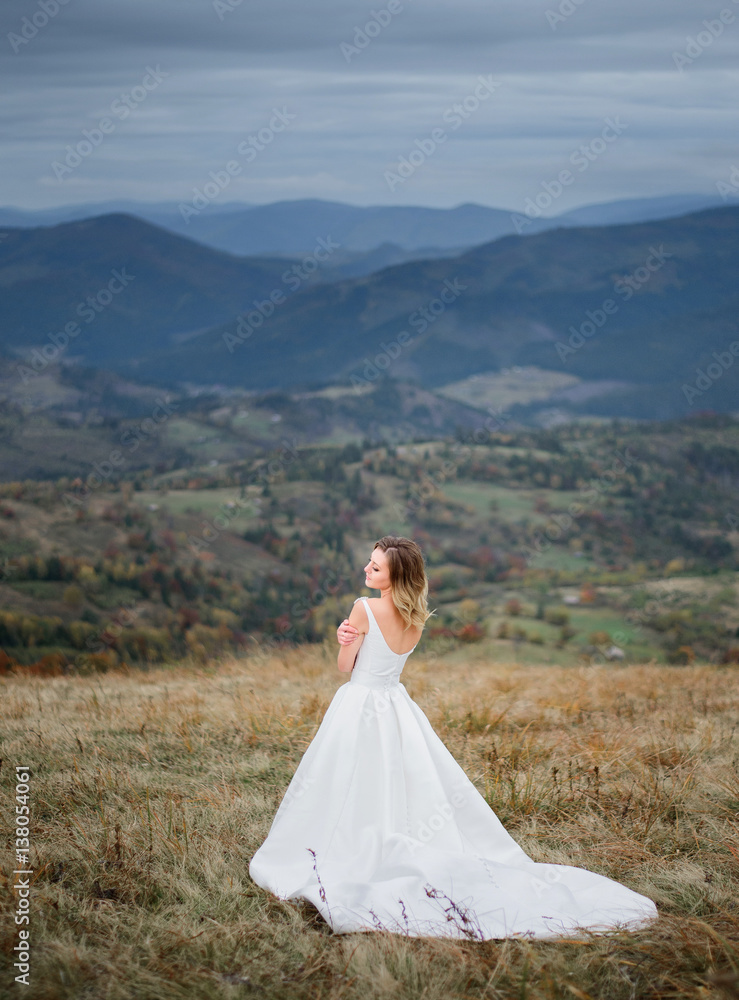 Bride holds her shoulders tender standing on the hill among the mountains Bride holds her shoulders tender standing on the hill among the mountains