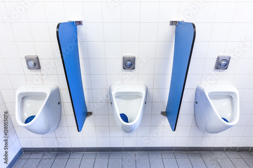 Urinals for men on white wall with blue partitions photo