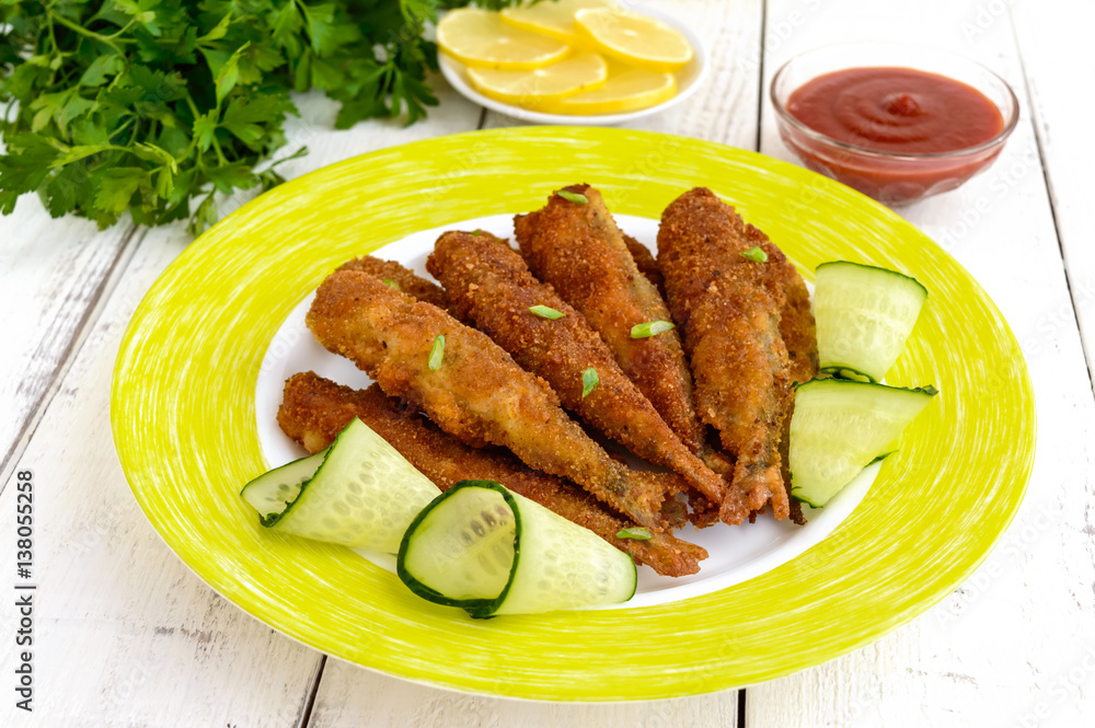 Deep frying small fish capelin on a plate on white wooden background. Deep frying small fish capelin on a plate on white wooden background.